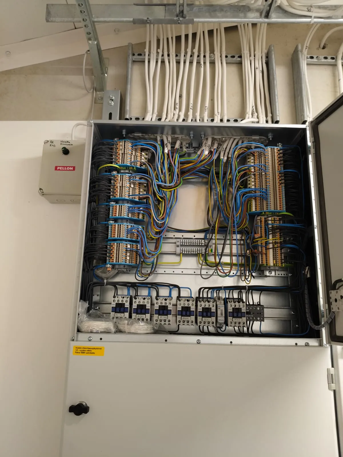 Sähkötaulu, jossa avoin ovi paljastaa järjestelmällisesti järjestetyt johdot ja sähkökomponentit monivärisillä johdoilla.
